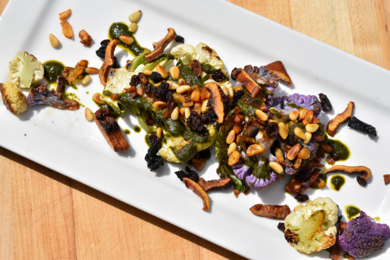 Charred cauliflower steaks, with sauce and toppings, served on a white dish