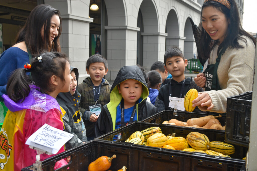 Foodwise volunteer, Kat, holds up a Delicata squash to show a group of Foodwise Kids at the Ferry Plaza Farmers Market.